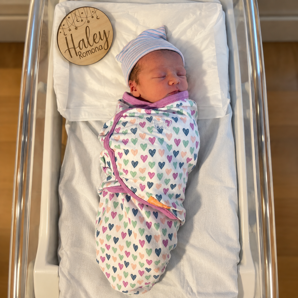 Newborn baby in hospital bassinet with personalized wooden name announcement sign