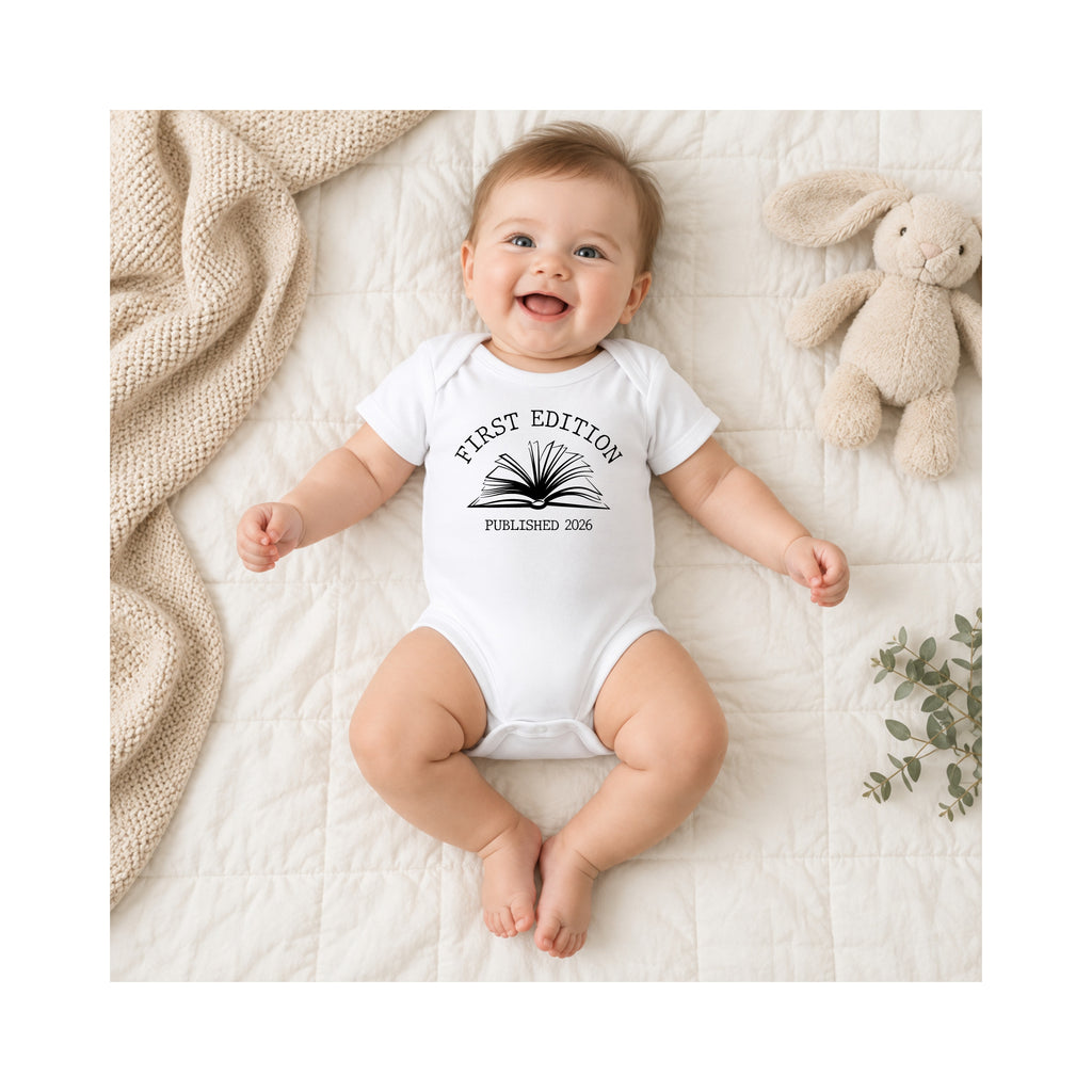 Smiling baby wearing white First Edition Published 2026 book baby bodysuit