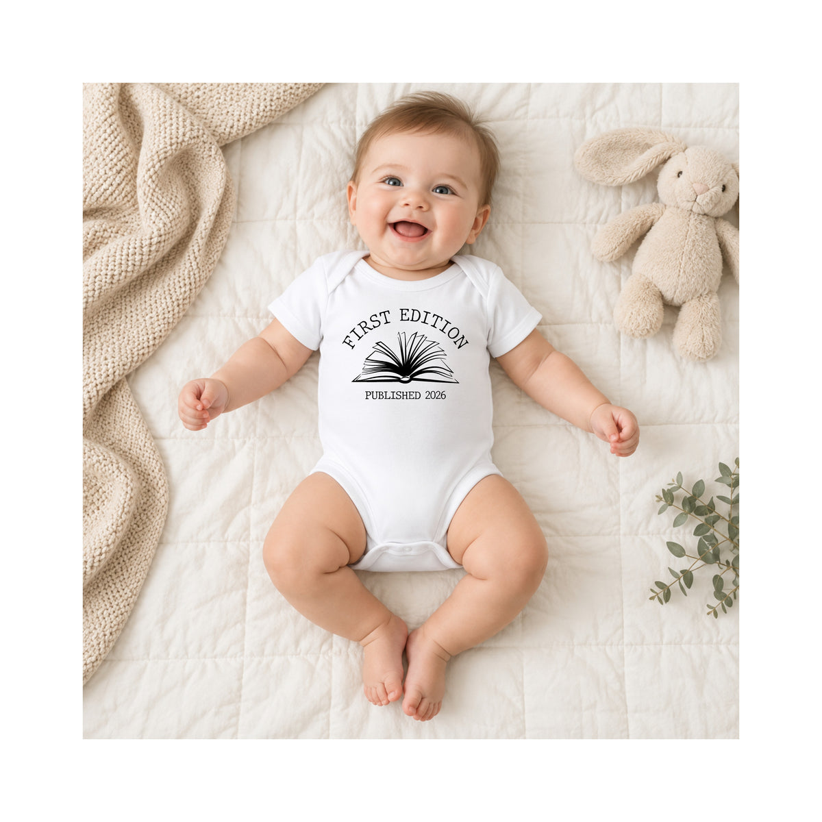 Smiling baby wearing white First Edition Published 2026 book baby bodysuit