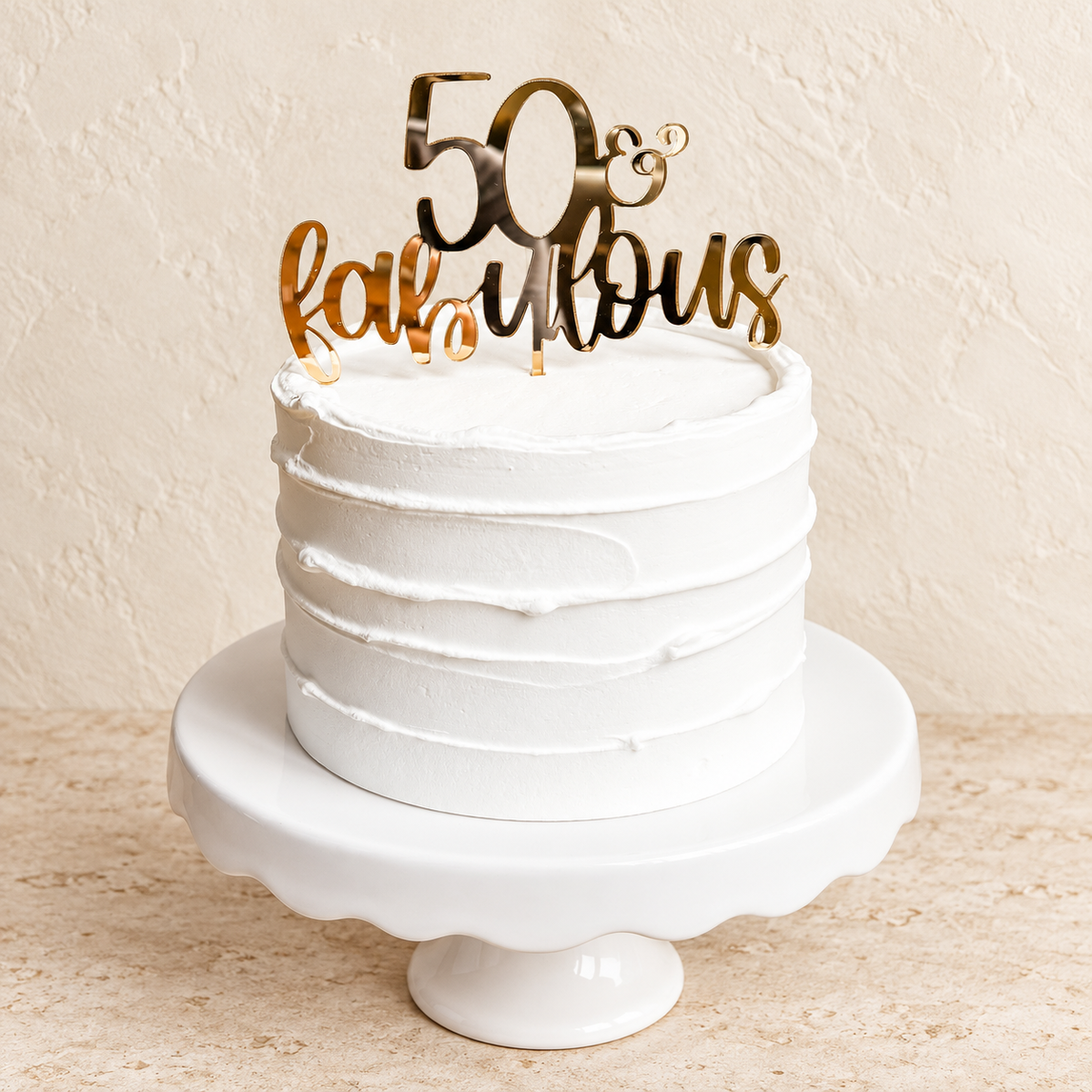 Gold 50 and fabulous mirrored acrylic cake topper on a white birthday cake with a warm cream background