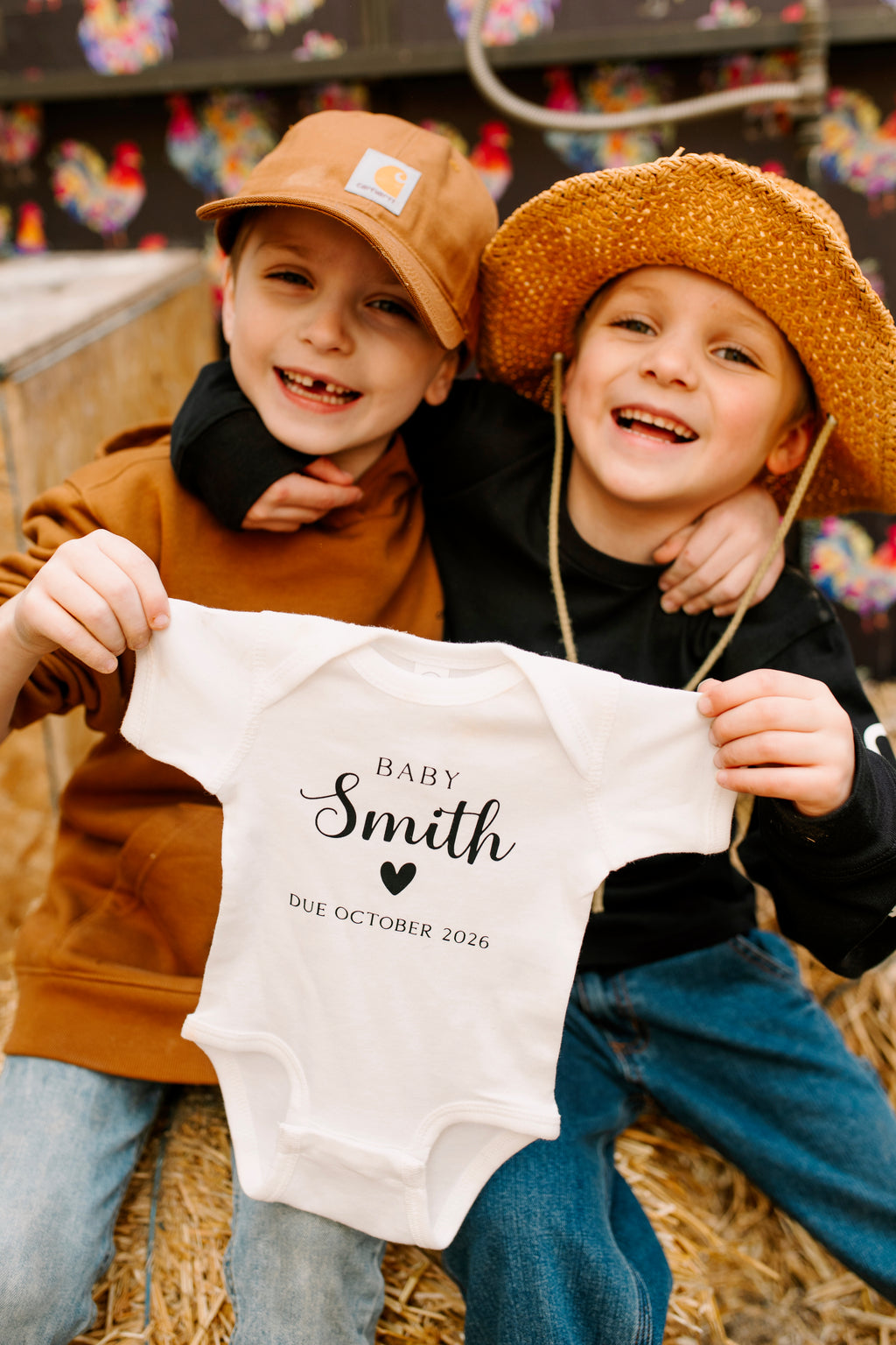 Siblings holding a personalized pregnancy announcement baby bodysuit